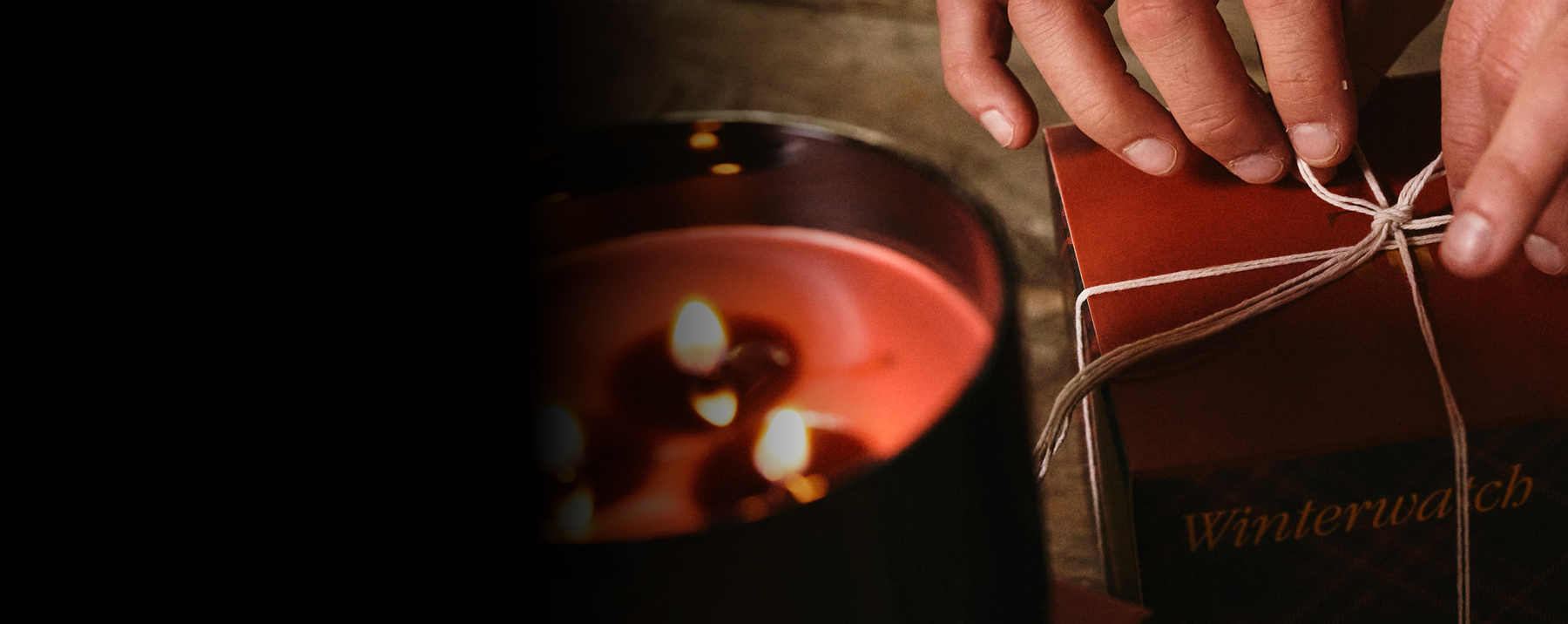 Person tying a string on a box labeled 'Winterwacht' with a warm, cozy background.